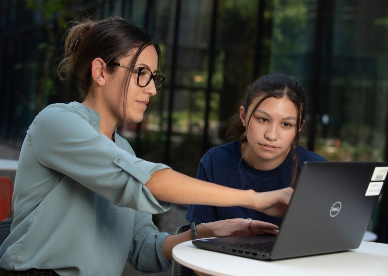  A mentor assists a student with a laptop, pointing to the screen during a one-on-one tutoring session in a bright, modern space.
