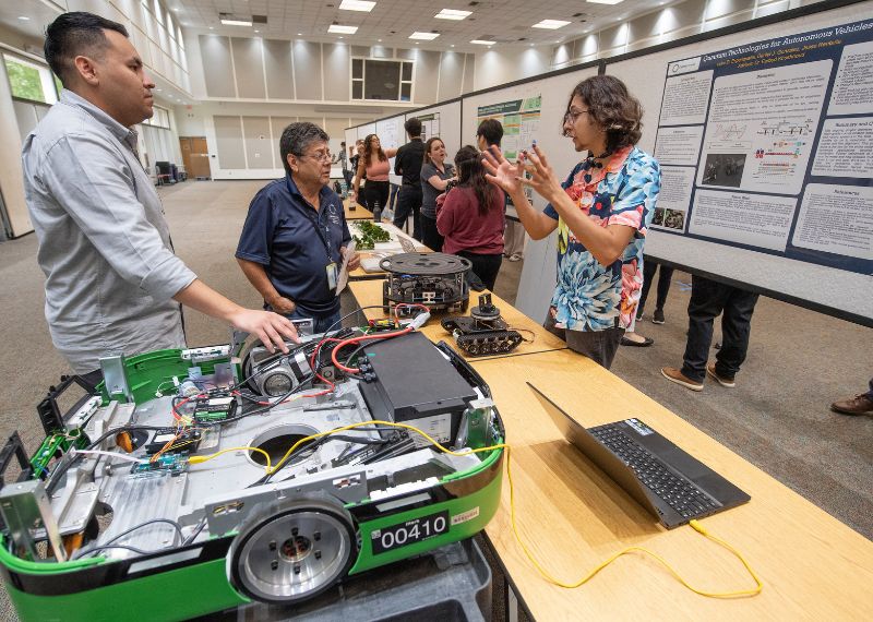 Undergraduate research student explains research poster to a person visiting their table.