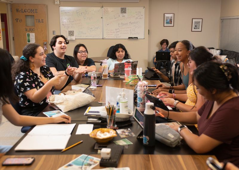  A group of students sits around a large table in a classroom, collaborating and discussing their work.