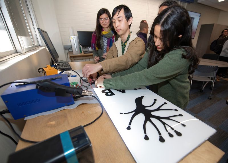 Students in a maker studio work together on a project involving a sign and tools.