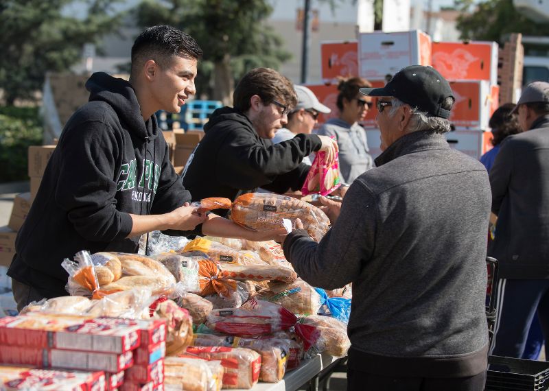 A young volunteer hands bread to an older man at an outdoor food distribution event.