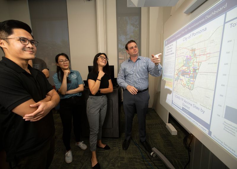 A presenter discusses a strategic dashboard displaying city data while students observe.