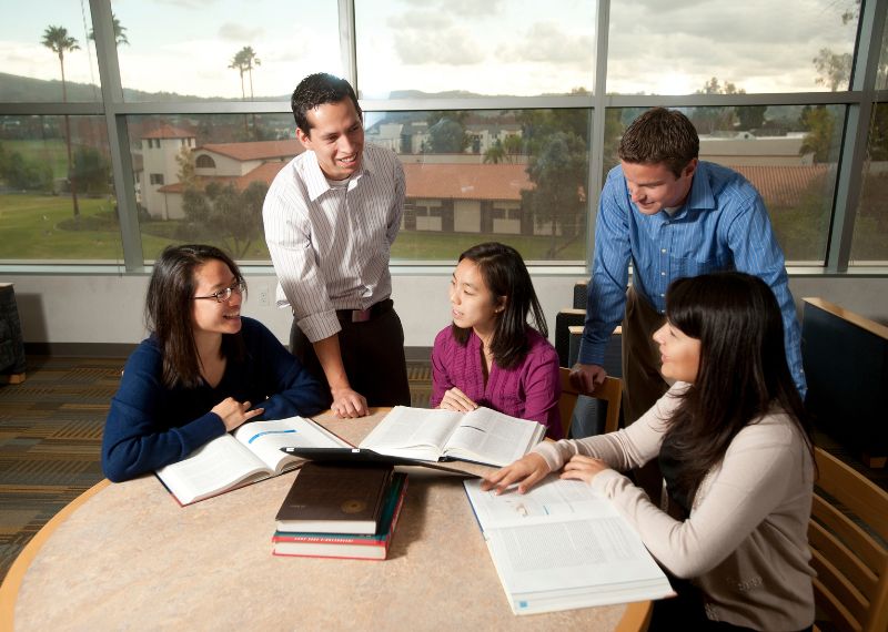 A diverse group of students collaborate in a study session at the library, discussing academic topics.