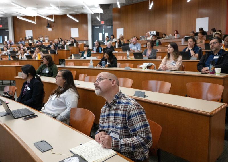 Faculty and staff attend an academic workshop in a lecture hall, engaging with speakers and taking notes.