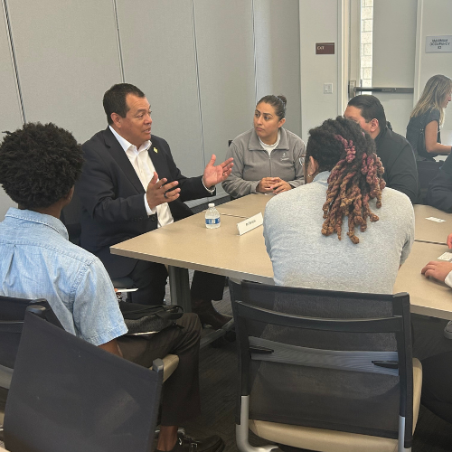 students gathered around a table listening to an alum share his career trajectory