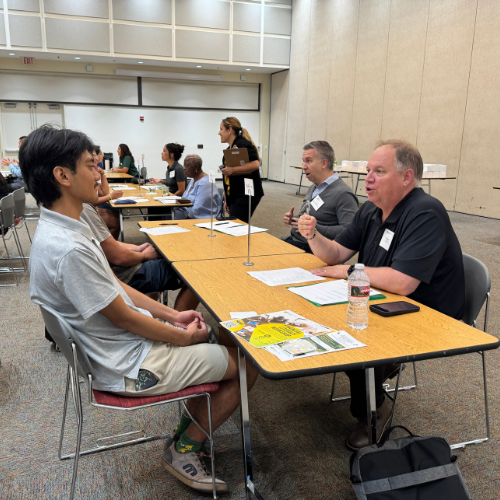 Two alumni and two students engaged in conversation at a table during a networking event.