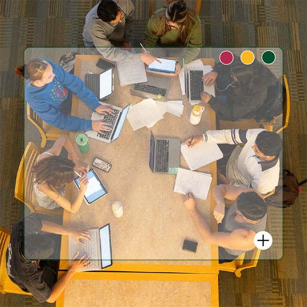 students studying at a table with laptops and mobile devices