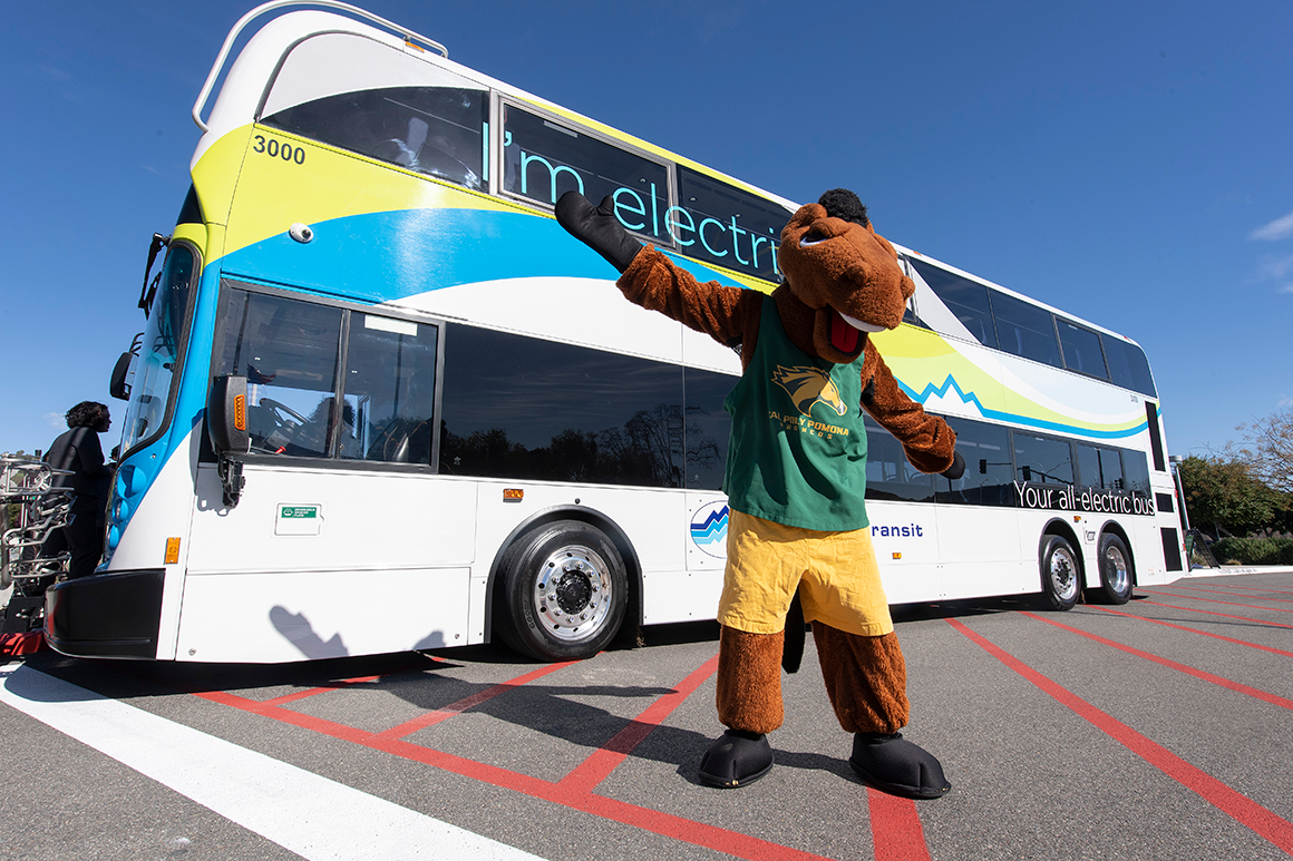 CPP mascot Billy Bronco stands in front of Silver Streak bus. 