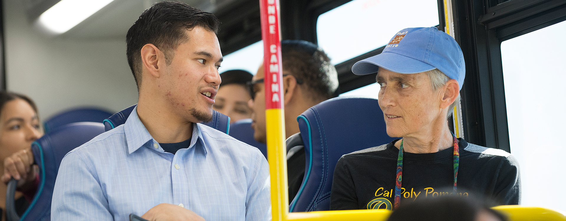 Two people speaking while sitting on a bus.