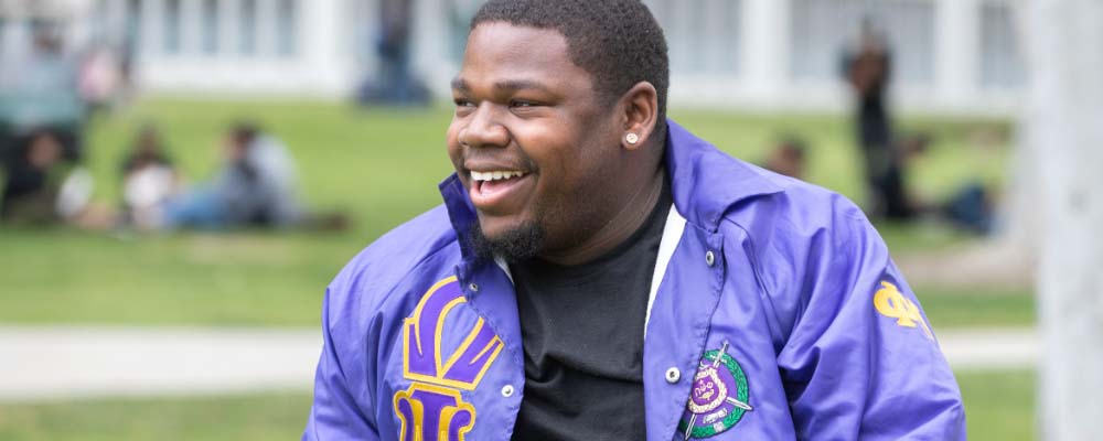 A Fraternity member smiles at the camera in his letterman jacket
