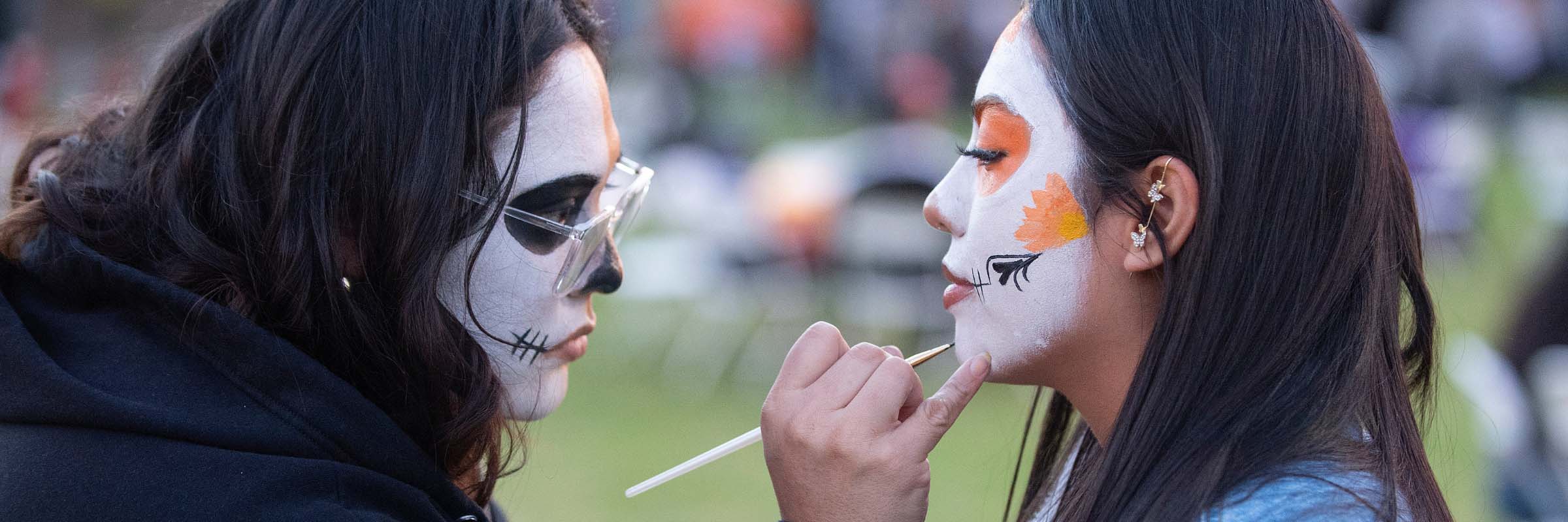 A face painter paints the face of a student at Dia de los Muertos