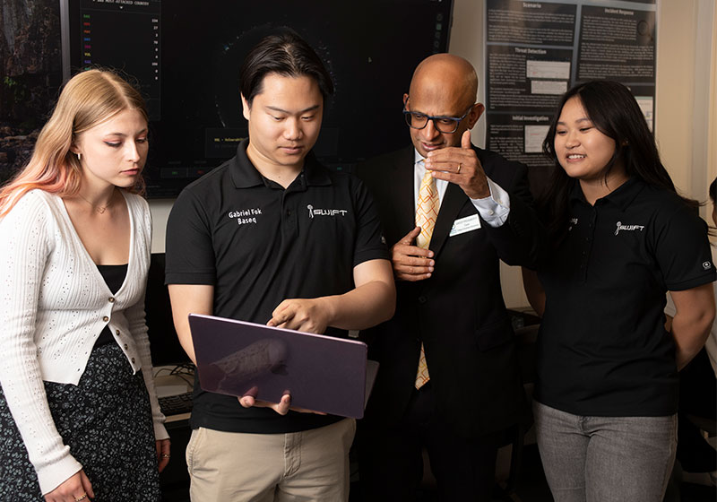 Dean Krishnamurthy with students in cybersecurity lab looking at laptop
