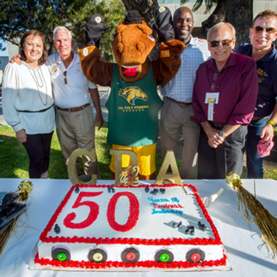 50th kickoff barbeque with Provost Alva, Billy Bronco and Class of 68 and 69 members next to 50 birthday cake