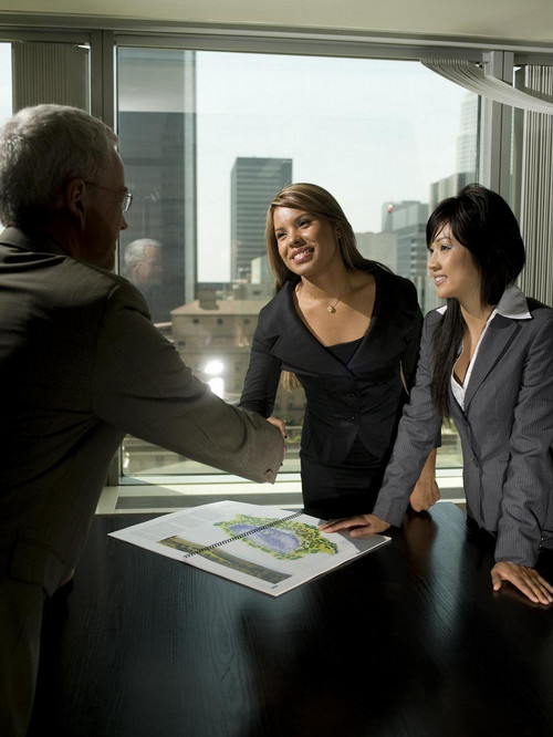 Business students shaking hand of executive in office overlooking city