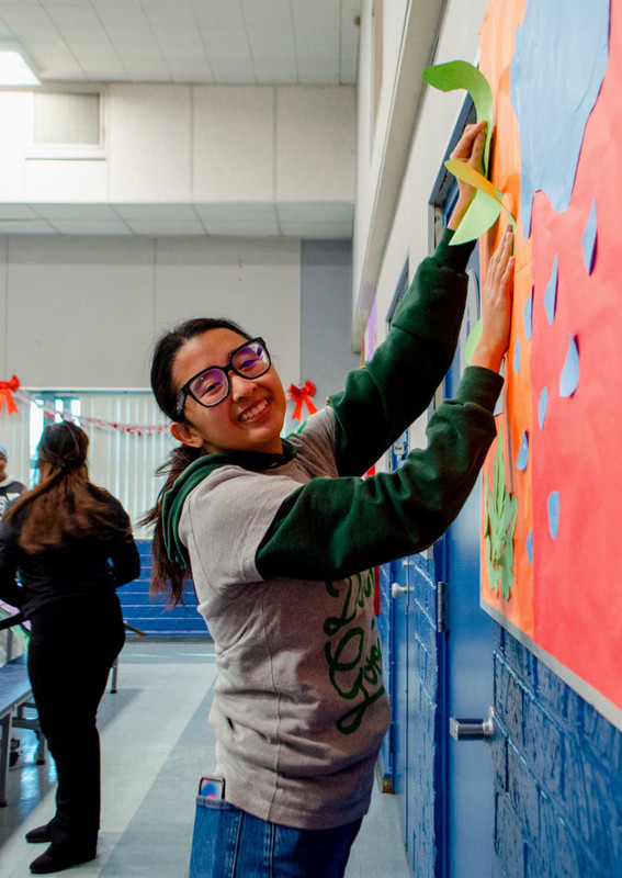 A woman reaching to staple a paper cut-out in the shape of cherries onto a wall