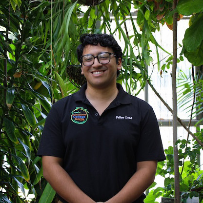 man in black shirt wearing glasses and smiling in front of plants