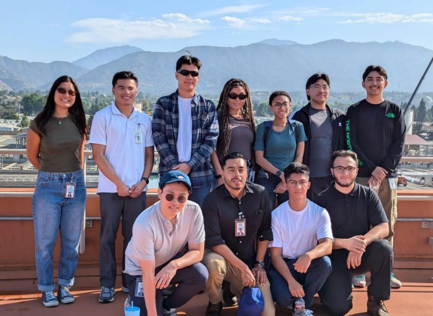 Group of eleven young adults on a rooftop with mountains in the background, smiling at the camera.