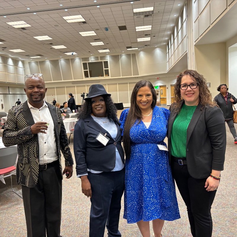 Group of Alumni at an event. One male and three female dressed in formal clothing standing together and smiling. 