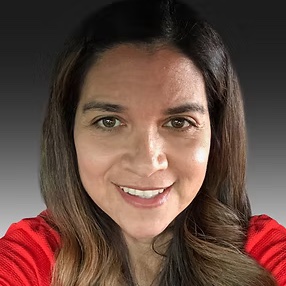 Female is a nature setting smiling big and showing her teeth. She has long curled hair. 