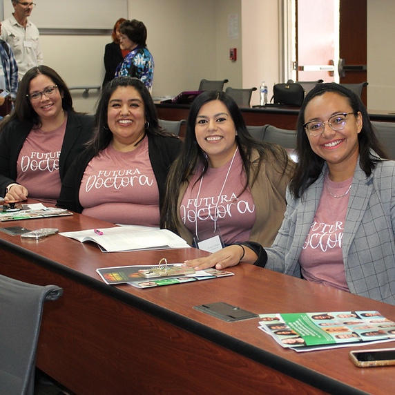Groups of Alumni in pink shirts sitting down and smiling. 
