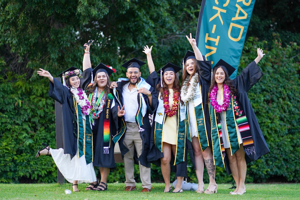 Students in regalia cheering at commencement behind a greenery. 