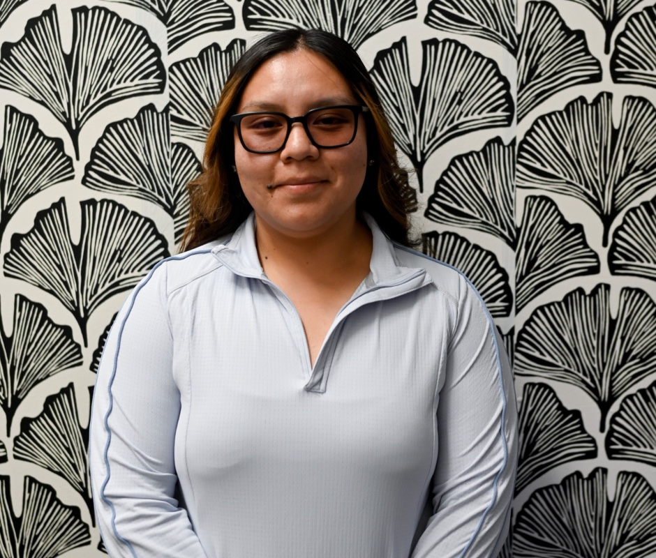 Female wearing blue sweater and glasses behind a black and white floral design background. 