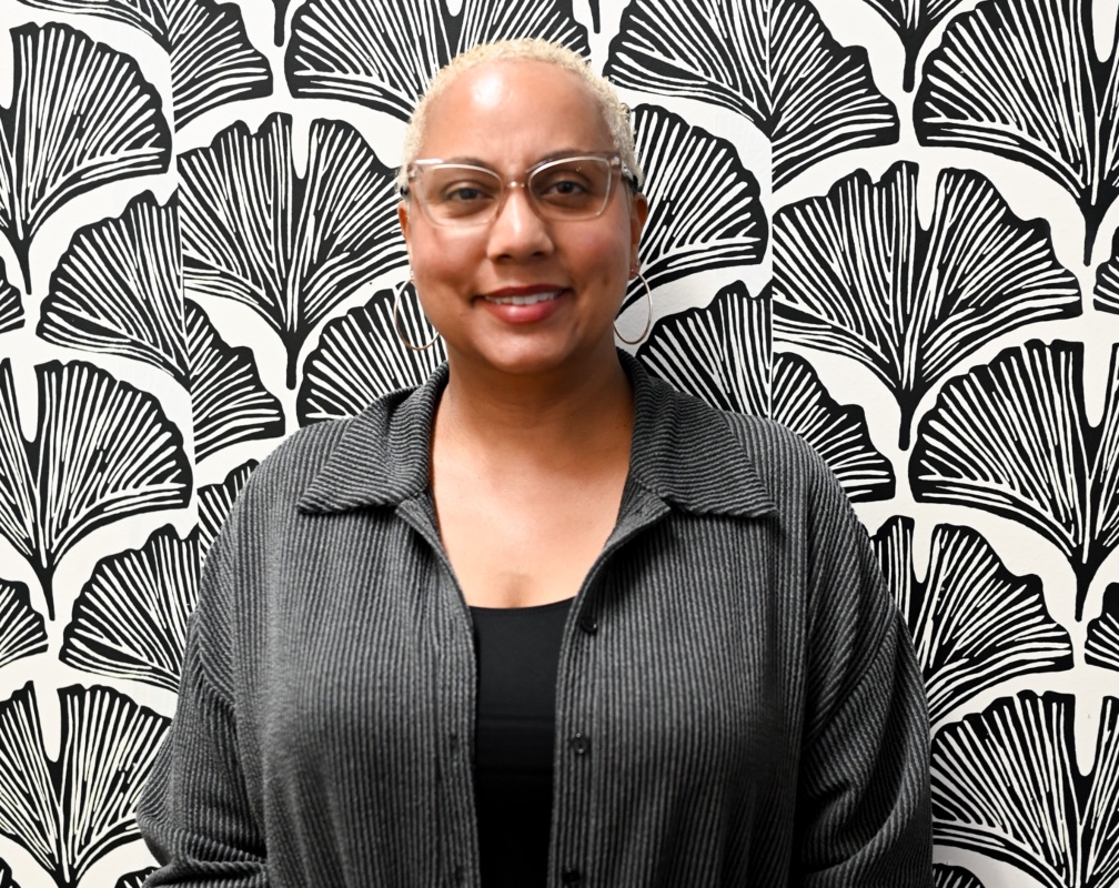 Female wearing grey top behind a black and white floral design background. 