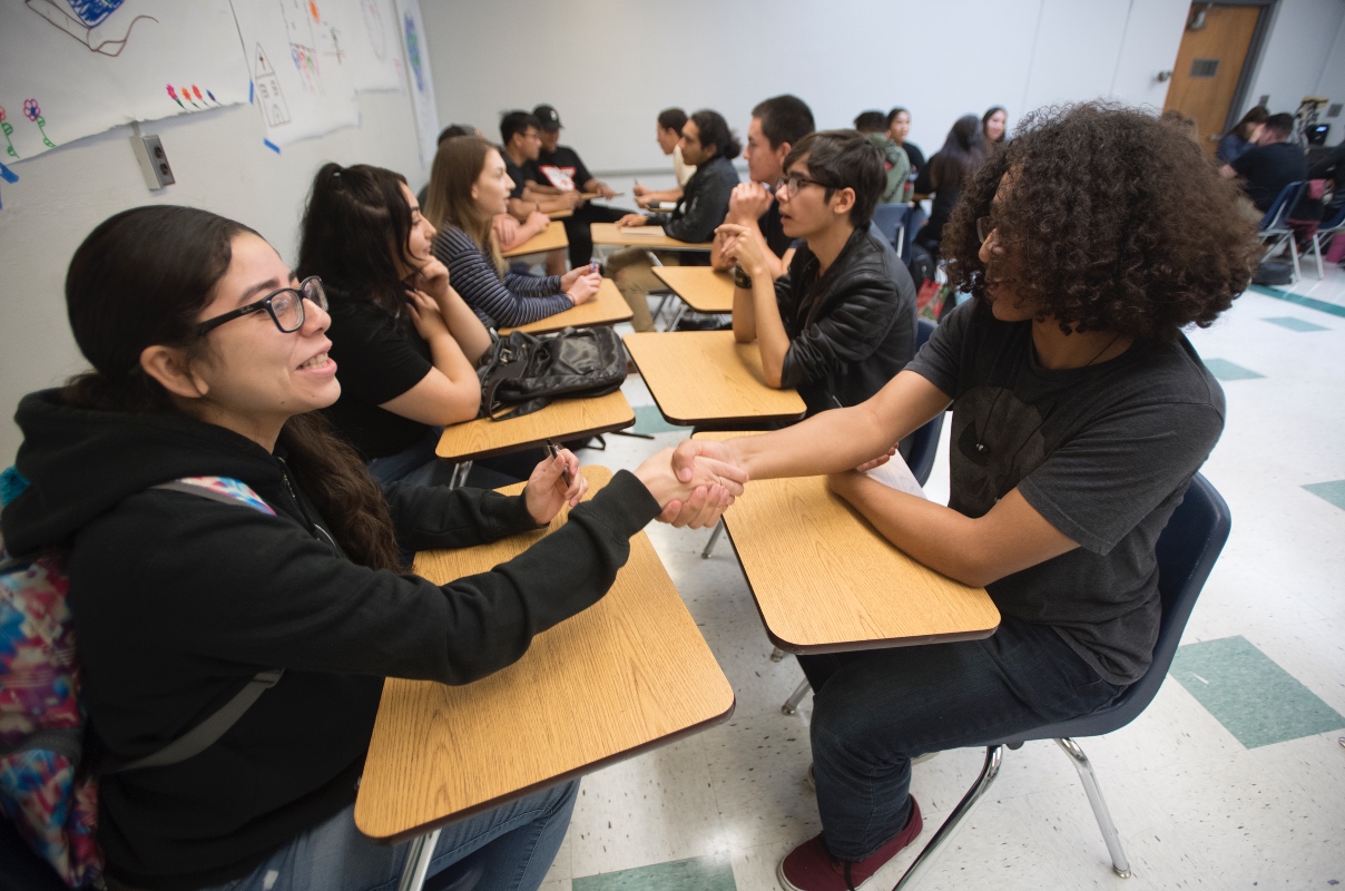 students in classroom facing each other and shaking hands. 