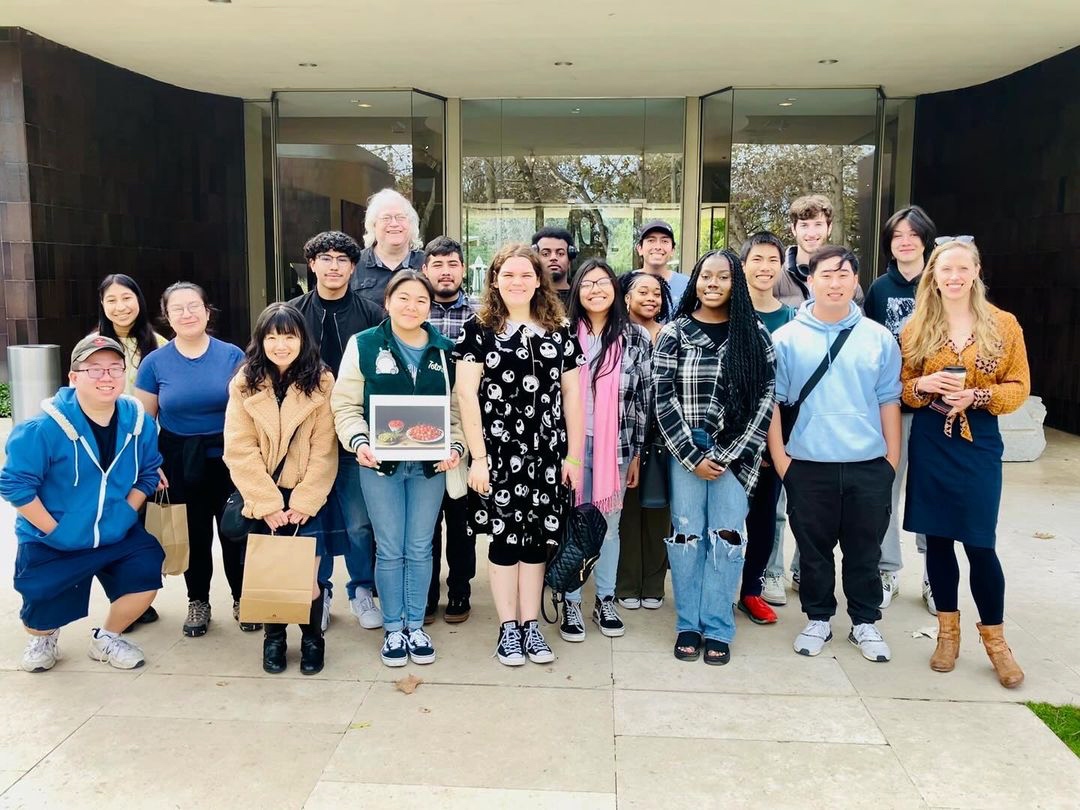 class standing in smiling outside of a museum.