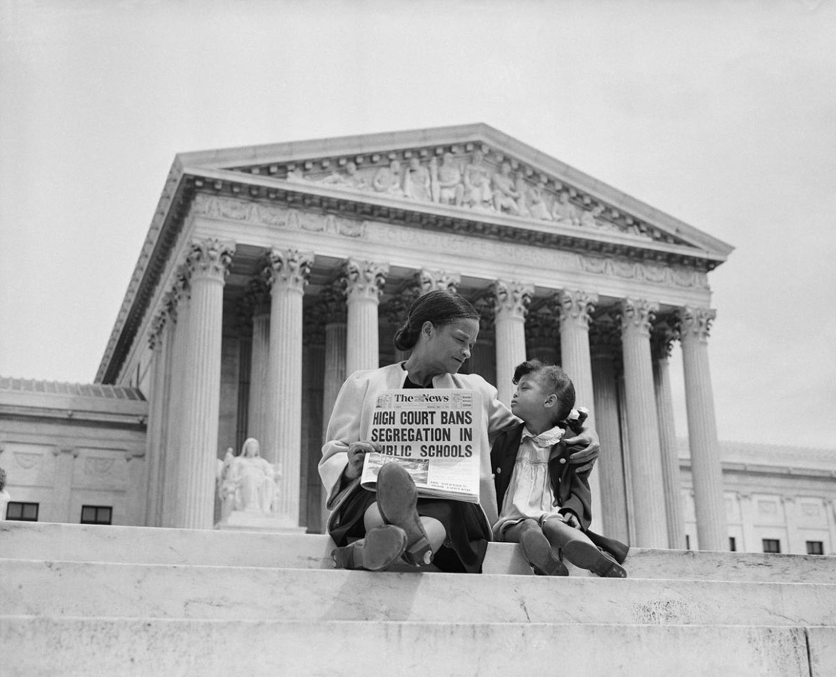 A woman and child sitting on the steps of the Supreme Court holding a newspaper announcing the end of segregation
