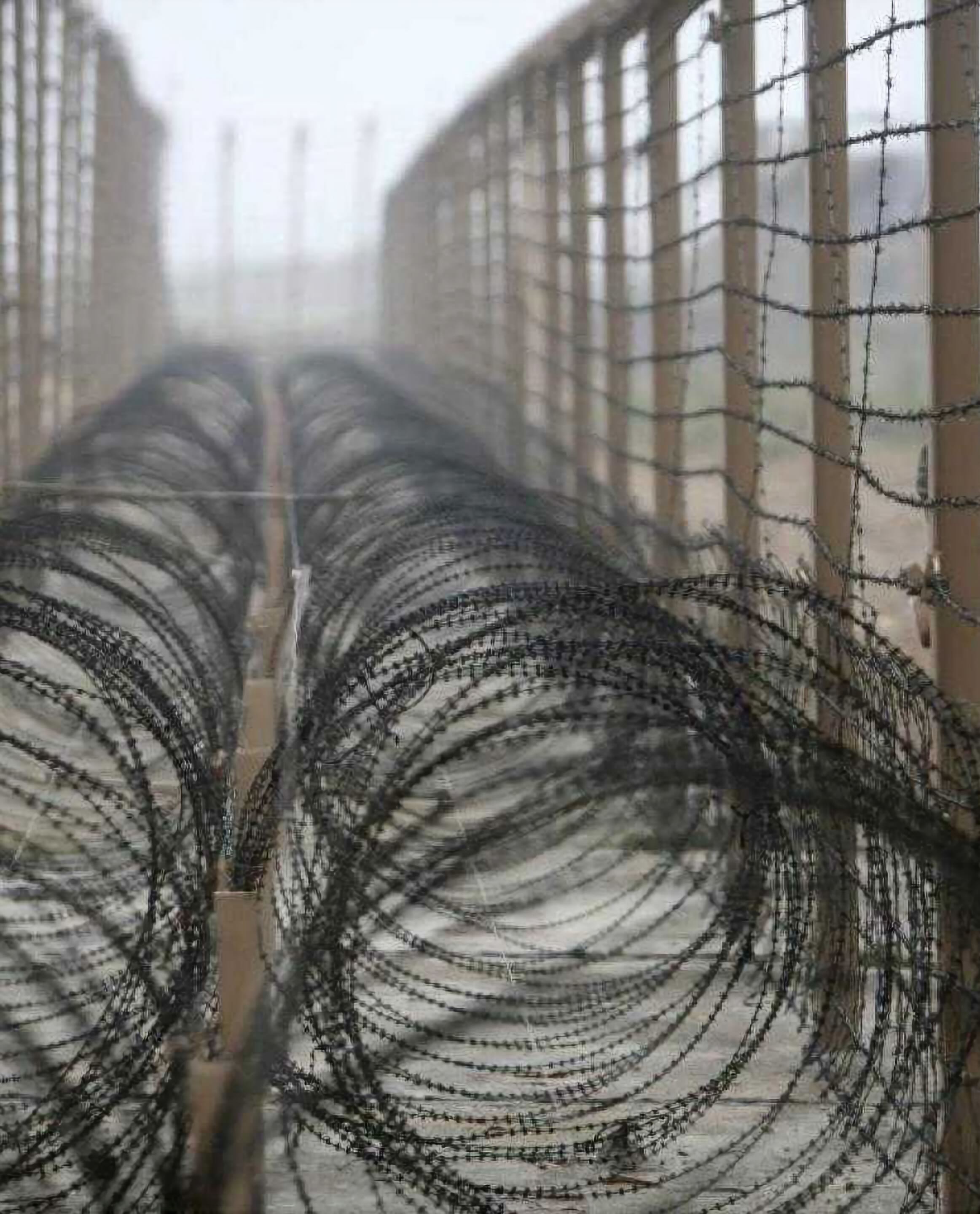 A dusty, brutal image of rolls of barbed wire at a nameless border