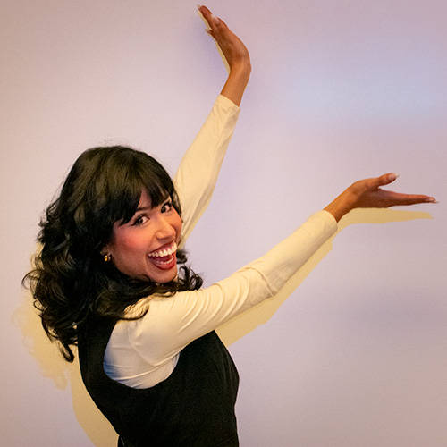 Smiling young woman gestures upward with two hands.