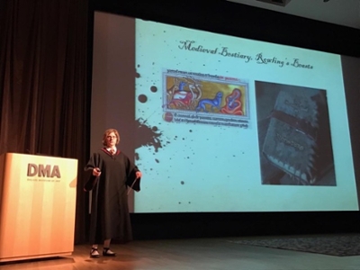Dr. Aaron talks on a stage in front of a projected slide with medieval beasts on it