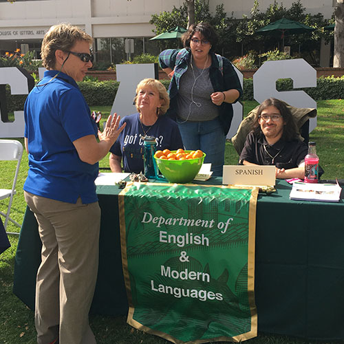 Picture taken outside Building 5. Associate Dean Sara Garver is standing at an information table staffed by EML department chair Liliane Fucaloro and two students, Maria Acero and Casey Marshall.