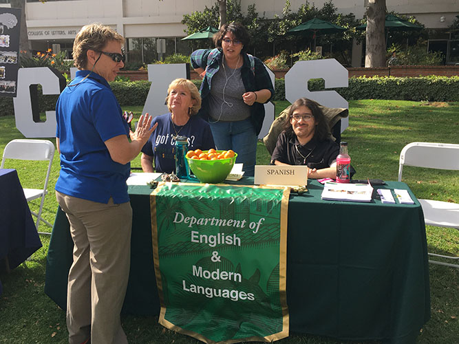 Picture taken outside Building 5. Associate Dean Sara Garver is standing at an information table staffed by EML department chair Liliane Fucaloro and two students, Maria Acero and Casey Marshall.
