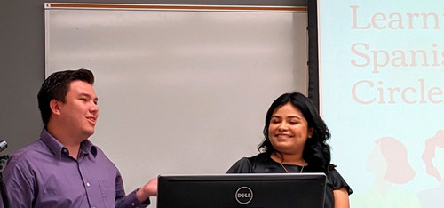 Two people smile in front of a slide projection about learning circles