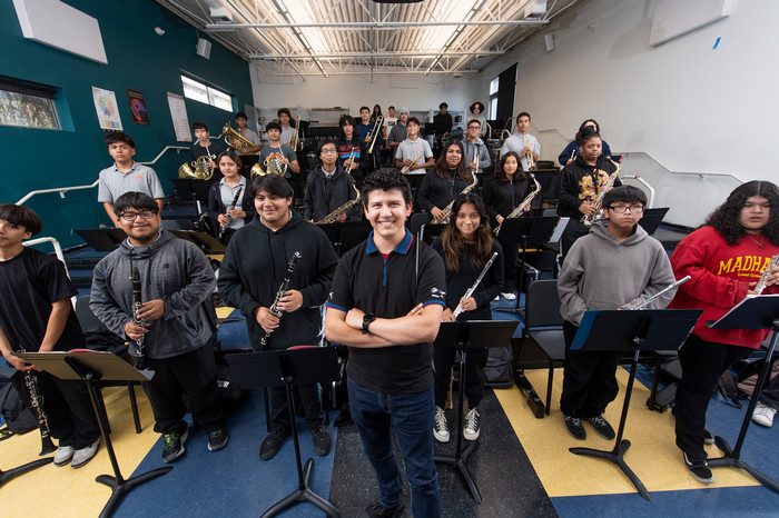 Band director and high school music students pose with instruments in a classroom rehearsal setting.
