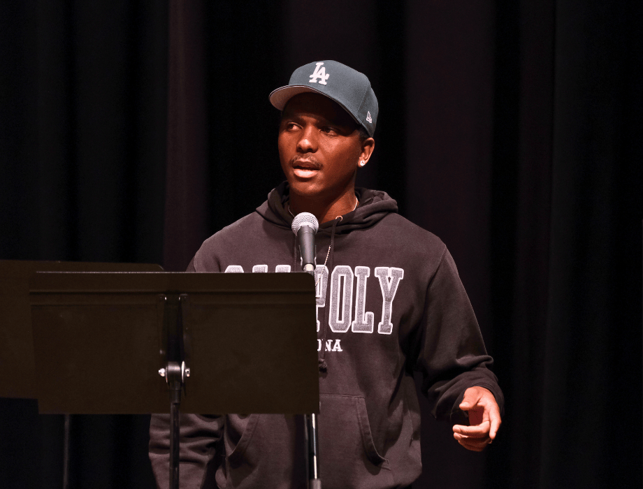 A student performs on stage wearing a Cal Poly Pomona hoodie, speaking or singing into a microphone during a showcase.