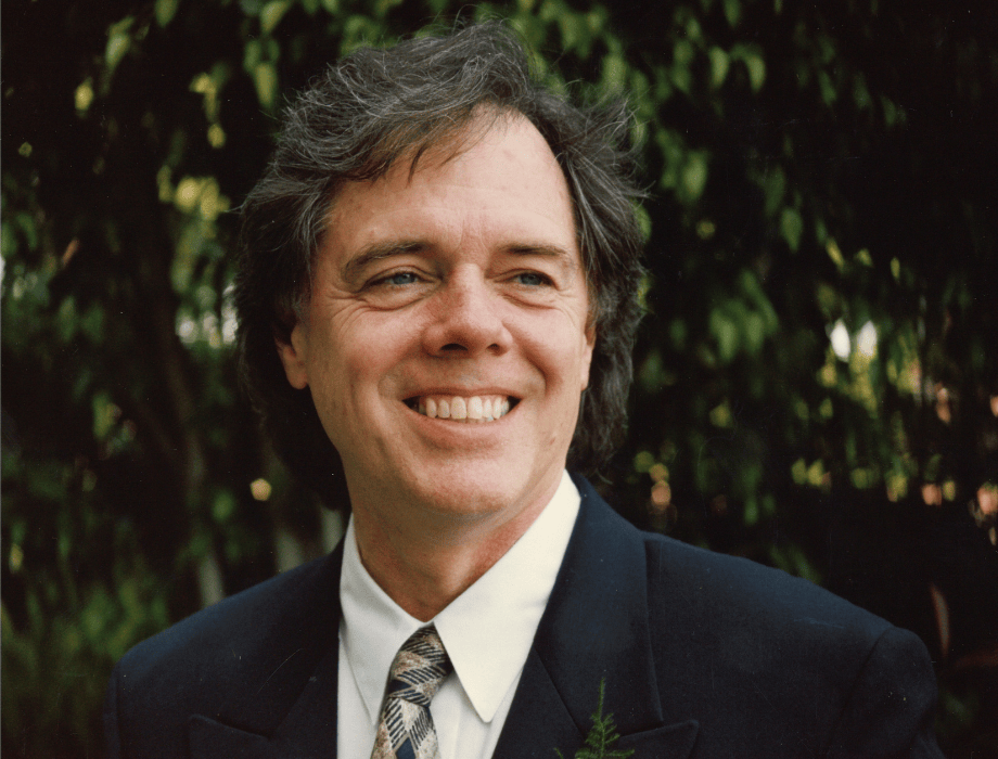 Portrait of composer and jazz musician Les Hooper smiling outdoors in a suit and tie.
