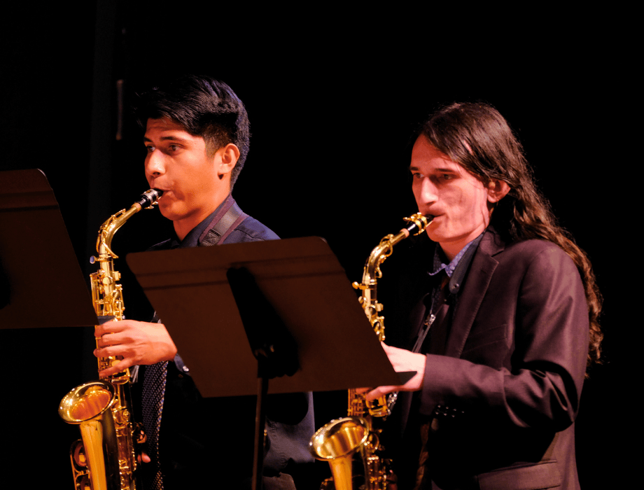 Two student musicians perform on stage, playing alto saxophones during an ensemble concert.