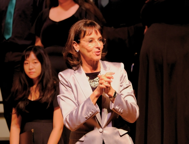 Faculty member speaking on stage in front of a choir during a music performance.