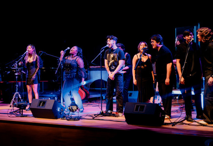CPP Music Industry Studies students perform a group vocal set on stage with a live band and lighting.