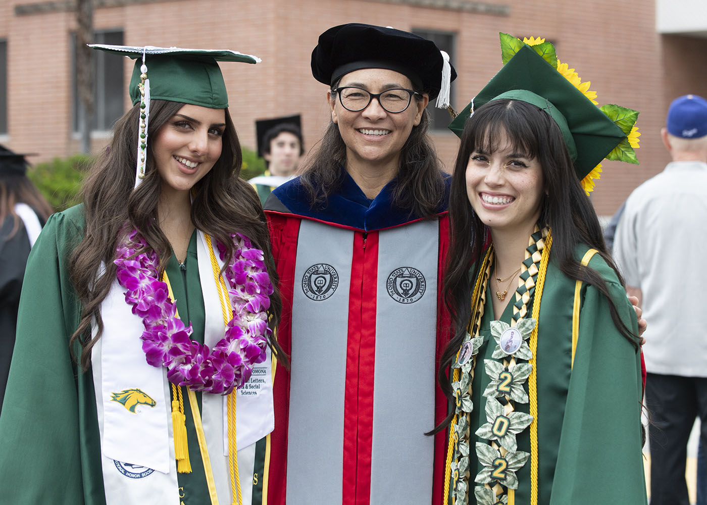 Two graduates pose with a faculty member during Cal Poly Pomona commencement.
