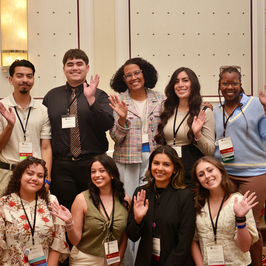 A group of students and a faculty member smile and wave at a conference.