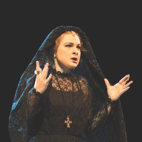 A student actor performs with passion in a theatre production, wearing a black veil headress.