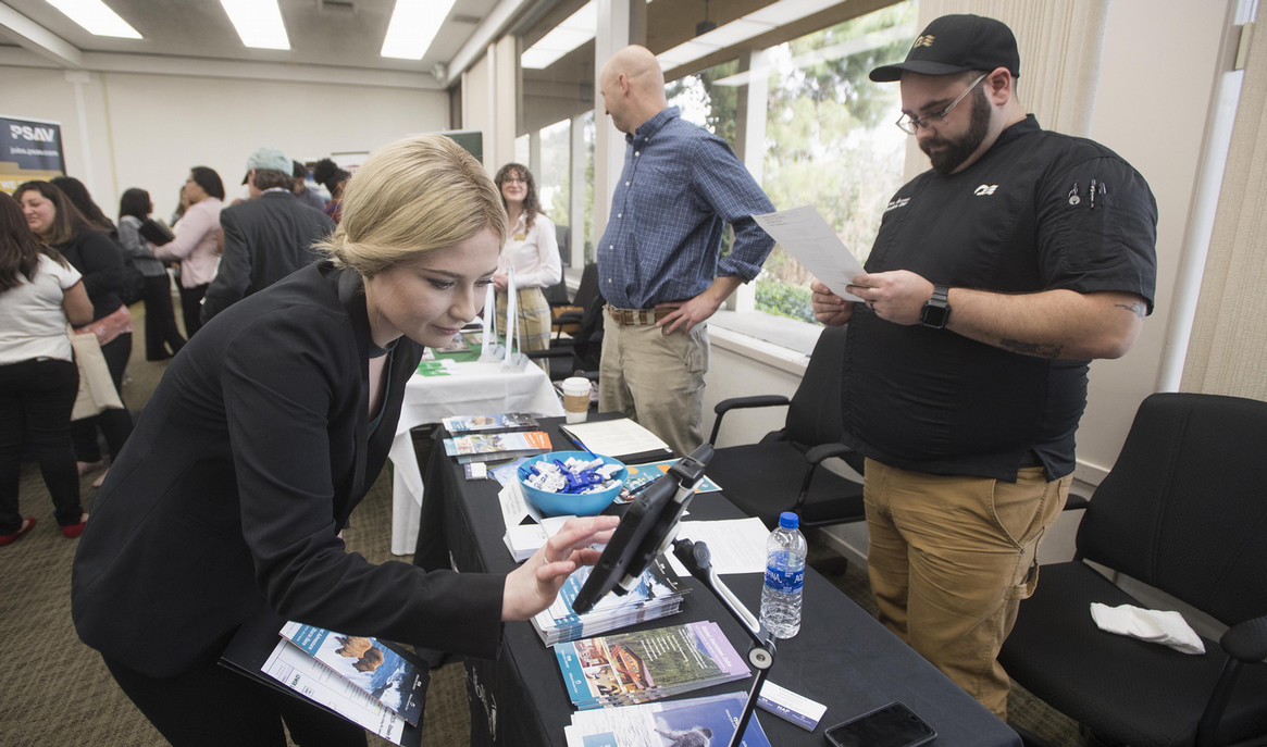 Student leaning over a table at the Hospitality Career Expo interacting with an electronic tablet.