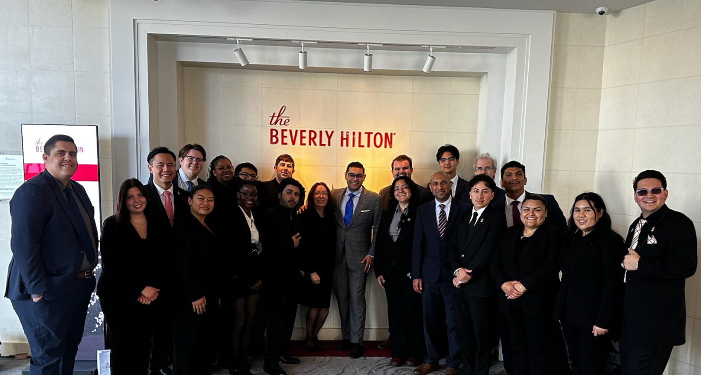 A group picture of students in formal attire underneath a painted wall sign that says Beverly Hilton