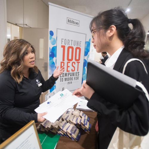 A student meeting a Hilton representative at the hospitality expo over a table indoors.