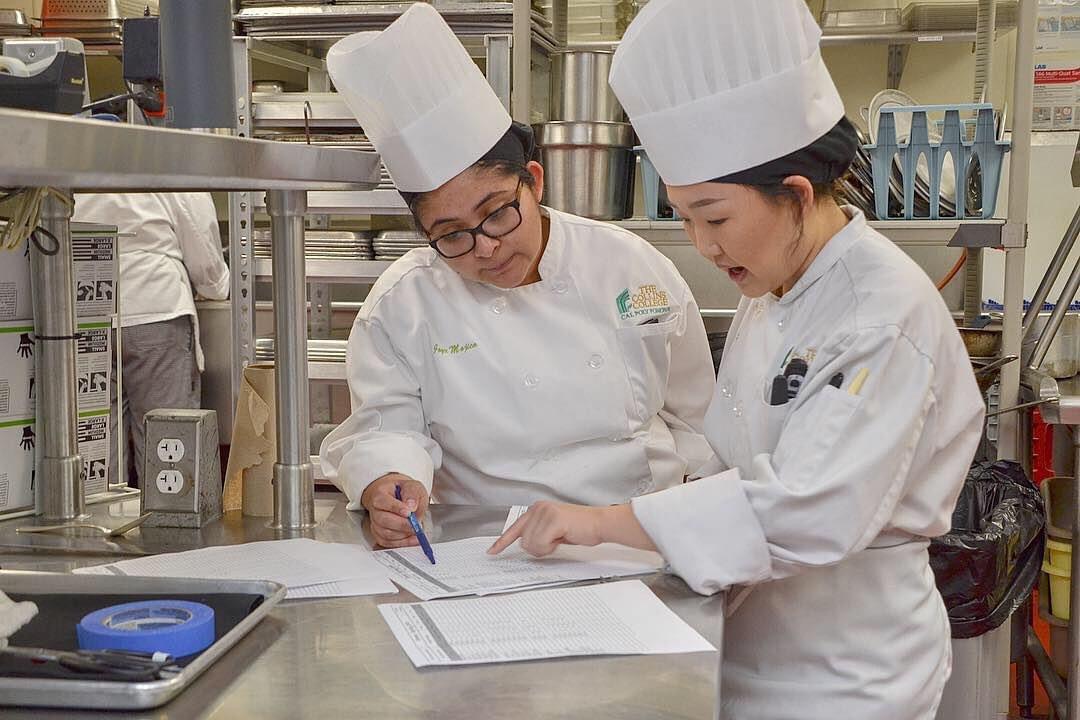 two students in chef coats calculating numbers on paper.
