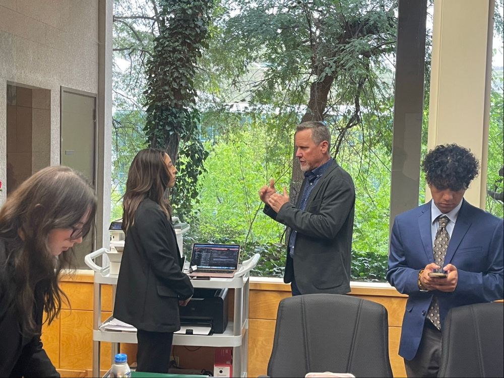 Students in a conference room talking to a professional in front of a large window.